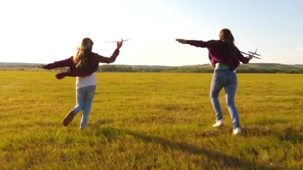 Όνειρα πτήσης. Χαρούμενη παιδική ιδέα. Δύο κορίτσια παίζουν με ένα παιχνίδι αεροπλάνο στο ηλιοβασίλεμα. Παιδιά στο φόντο του ήλιου με ένα αεροπλάνο στο χέρι. Σιλουέτα παιδιών που παίζουν στο αεροπλάνο — Αρχείο Βίντεο