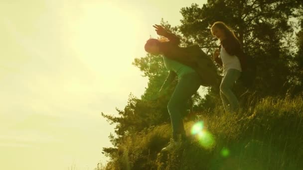 Wanderin. Touristen Teamwork. Wandermädchen steigen vom Berg herab. Touristenfamilie bei Sonnenuntergang unterwegs. Schwestern mit Rucksäcken fahren in der Sonne bergab. — Stockvideo