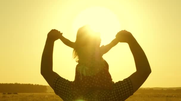 Pai brinca com a criança ao sol. conceito de infância feliz. pequena filha montando com o pai em seus ombros no parque. Pai carrega bebê amado em seus ombros andando em torno do campo ao pôr do sol — Vídeo de Stock