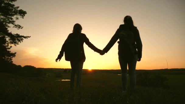 Vrouwen reizen, houden elkaars hand vast, lopen bij zonsondergang door het bos. Wandelmeisje. Langzame beweging. Meisjesreizigers gaan naar de klif en genieten van de zonsondergang. teamwork van toeristen. sport toerisme concept. — Stockvideo