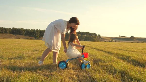 Mamma lär dotter att rida en cykel. dotter och mor spelar på ängen. Mamma leker med sin lilla dotter. ett litet barn lär sig att cykla. begreppet lycklig barndom. — Stockfoto