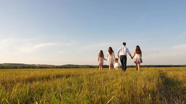 Madre, padre e hija pequeña con hermanas caminando en el campo bajo el sol. Feliz familia joven. Los niños, papá y mamá juegan en el prado bajo el sol. concepto de una familia feliz . —  Fotos de Stock