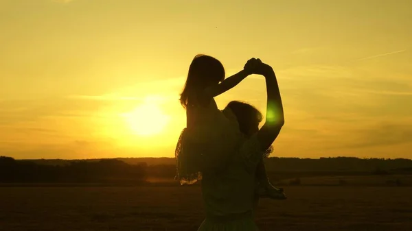 Mãe feliz e bebê caminham pelo campo ao pôr do sol e riem. Uma menina senta-se sobre os ombros de sua mãe e caminha junto no parque ao sol e sorri. Conceito de vida familiar. Movimento lento — Fotografia de Stock