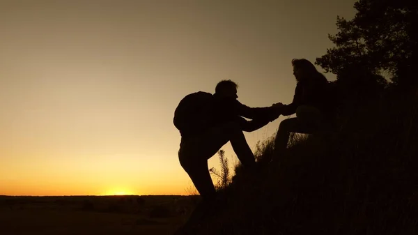 女性旅行者は丘の上に登るのを助ける男性旅行者の手を握っています。観光客の手を握って、日没で山に登る。ビジネスパートナーのチームワークです休暇中の幸せな家族. — ストック写真