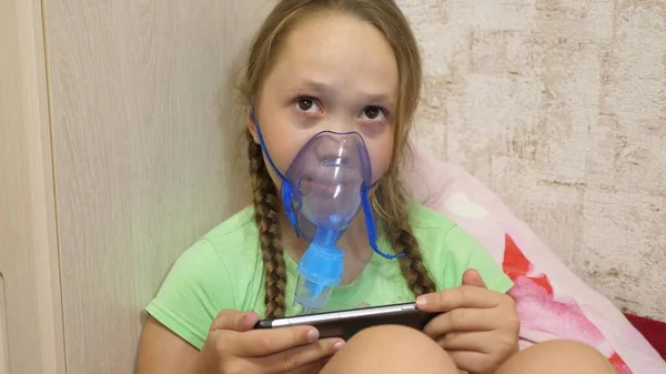 child with tablet is sick and breathes through an inhaler. close-up. little girl treated with an inhalation mask on her face in hospital. Toddler treats flu by inhaling inhalation vapor.