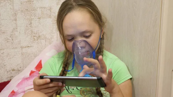 Niña pequeña tratada con una máscara de inhalación en su cara en el hospital. niño con un comprimido está enfermo y respira a través de un inhalador. Primer plano. El niño pequeño trata la gripe inhalando vapor de inhalación . —  Fotos de Stock