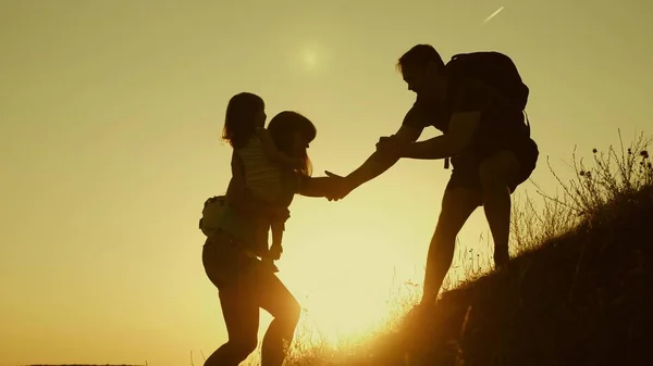 Πατέρας του κρατά το χέρι του βοηθώντας τα παιδιά να σκαρφαλώσουν στο βουνό. Οικογένεια τουριστών με παιδιά που ταξιδεύουν το ηλιοβασίλεμα. μπαμπάς, τα παιδιά και η μαμά με σακίδια ταξίδι αναρρίχηση βουνό στον ήλιο. τουριστική ομαδική εργασία — Φωτογραφία Αρχείου