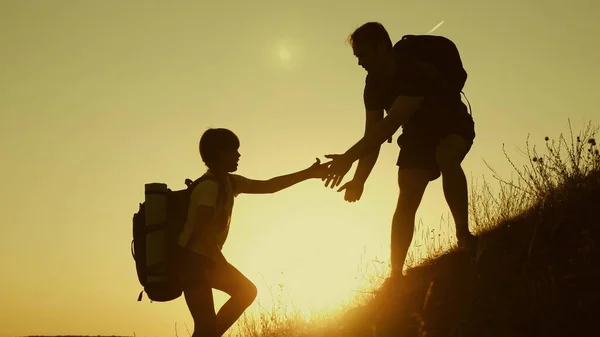 父は子供たちが山に登るのを手伝うのを手を差し出す。日没時に旅行する子供と観光客の家族。バックパックを持つお父さん、子供とママは、太陽の下で山を登ります。観光チームワーク — ストック写真