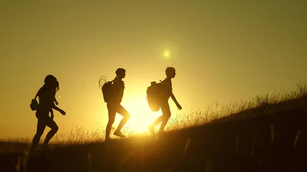 Bambini e mamma con zaini viaggiano scalano la montagna al sole. mamma e figlie vanno in campeggio. Famiglia di turisti con bambini che viaggiano al tramonto. lavoro congiunto dei turisti. movimento verso la vittoria . — Foto Stock