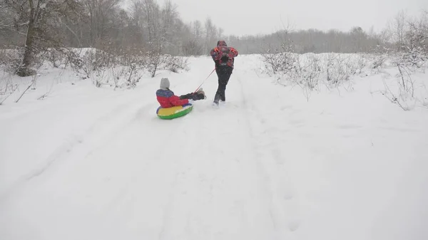 Pai feliz trenó uma criança em uma estrada nevada. Férias de Natal. pai brinca com sua filha em um parque de inverno. O conceito de uma família feliz. adolescente experiências em Tubing — Fotografia de Stock