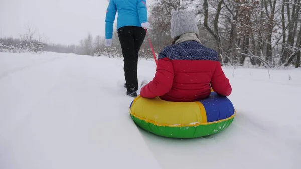 Niño y madre en trineo en la nieve. Hija y mamá juegan en el parque de invierno en las vacaciones de Navidad. vacaciones de invierno familiares. concepto de infancia feliz — Foto de Stock