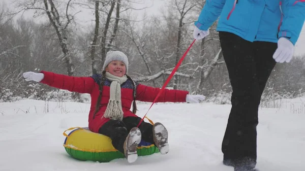 Kind und Mutter rodeln im Schnee. Tochter und Mutter spielen an den Weihnachtsfeiertagen im Winterpark. Winterurlaub für Familien. Konzept der glücklichen Kindheit — Stockfoto