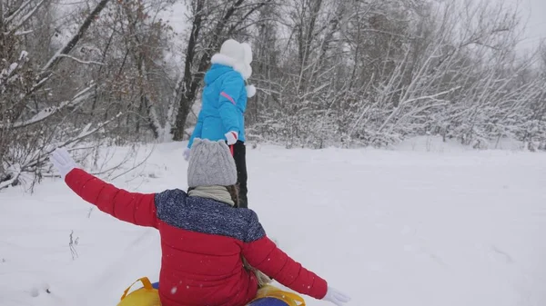 Vacaciones de invierno familiares. niño y madre en trineo en la nieve. Hija y mamá juegan en el parque de invierno en las vacaciones de Navidad. concepto de infancia feliz —  Fotos de Stock