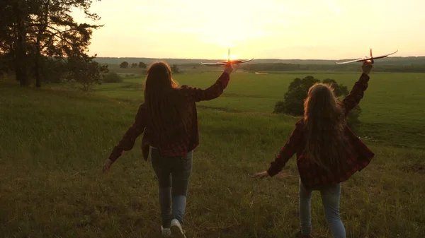 Träume vom Fliegen. Glückliche Kindheit. Zwei Mädchen spielen bei Sonnenuntergang mit einem Spielzeugflugzeug. Kinder im Hintergrund der Sonne mit einem Flugzeug in der Hand. Silhouette von Kindern, die im Flugzeug spielen — Stockfoto