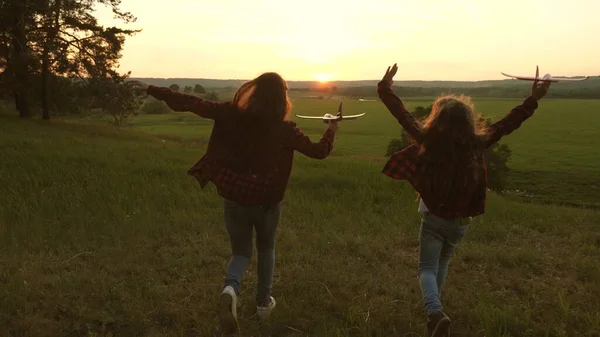 Dromen van vliegen. Gelukkige kindertijd concept. Twee meisjes spelen met een speelgoedvliegtuig bij zonsondergang. Kinderen op de achtergrond van de zon met een vliegtuig in de hand. Silhouet van spelende kinderen in het vliegtuig — Stockfoto