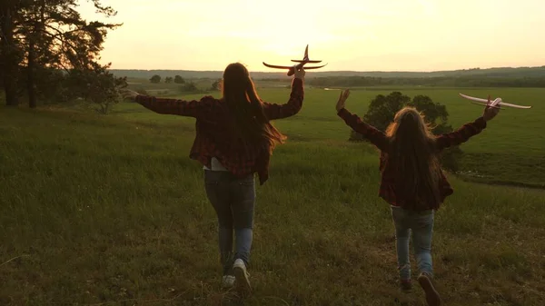 Drömmar om att flyga. Glad barndomsidé. Två flickor leker med ett leksaksplan vid solnedgången. Barn på bakgrunden av solen med ett flygplan i handen. Silhuett av barn som leker på planet — Stockfoto
