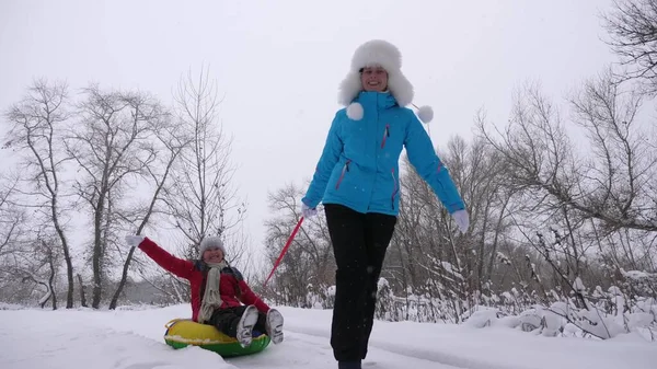 Семейные зимние каникулы. ребенок и мать катаются на санках в снегу. Дочь и мама играют в зимнем парке на рождественские каникулы. Концепция счастливого детства — стоковое фото