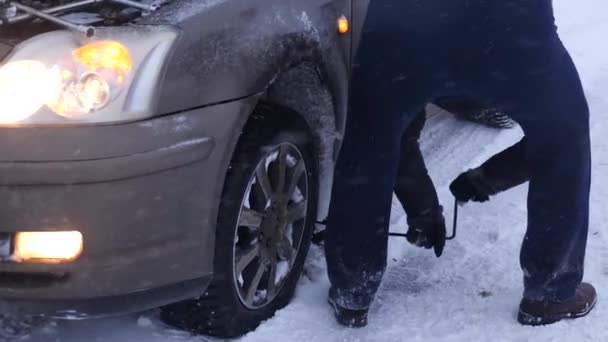 Hombre levanta gato de coche en la carretera. El hombre está cambiando la rueda del coche. ruedas de repuesto en invierno en carretera en una ventisca y nevadas. Desglose del coche, cambio de rueda . — Vídeo de stock