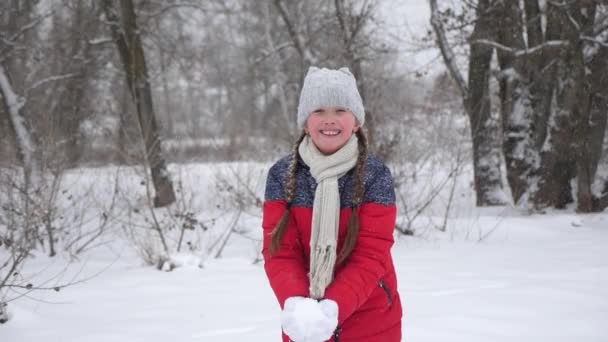 幸せな子供が雪を投げ、笑顔。クリスマス休暇旅行や休暇。雪の楽しさとゲーム。冬の森で休暇中の女の子 — ストック動画
