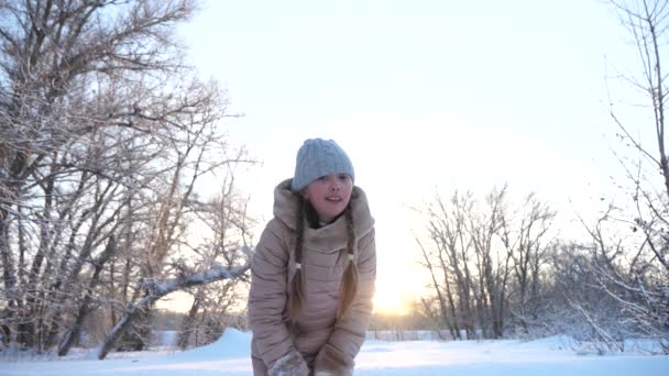 Il bambino gioca in inverno in parco per vacanze di Natale lancia la neve su. bambino gioca in inverno nel parco per le vacanze di Natale. Ragazza felice lancia fiocchi di neve al tramonto e sorride in un parco invernale. Lento. — Video Stock