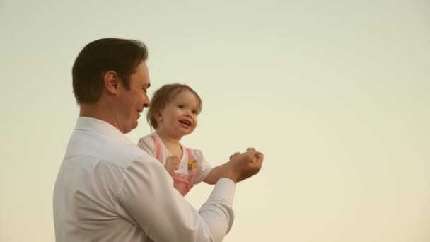 Papa dansen op zijn schouders met zijn dochter in de zon. Vader reist met baby op zijn schouders in stralen van zonsondergang. Een kind met ouders loopt bij zonsondergang. gelukkige familie rusten in Park. familieconcept — Stockvideo