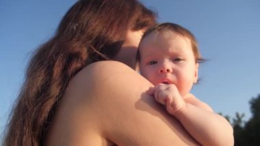 Anne sıcak bir yaz gününde mavi gökyüzüne karşı kucağında küçük bir bebek tutuyor. Dinlen ve çocuklarla seyahat et. Ebeveynle mutlu bir çocukluk. Mutlu aile kavramı. Yakın plan.