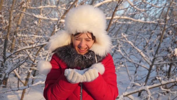 Niño feliz soplando copos de nieve al atardecer y sonriendo en el parque de invierno. En cámara lenta. Primer plano. niña sopla copos de nieve de sus manos, en el parque de invierno, iluminado por el atardecer . — Vídeo de stock