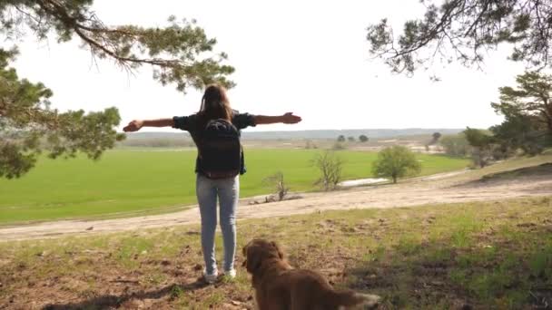 Reisenden mit einem Rucksack auf den Schultern und einem Hund, der seine Arme zur Seite ausbreitet und die Freiheit genießt. Der Hundezüchter geht mit seinem geliebten Hund spazieren. Mädchen meditiert im Freien. — Stockvideo