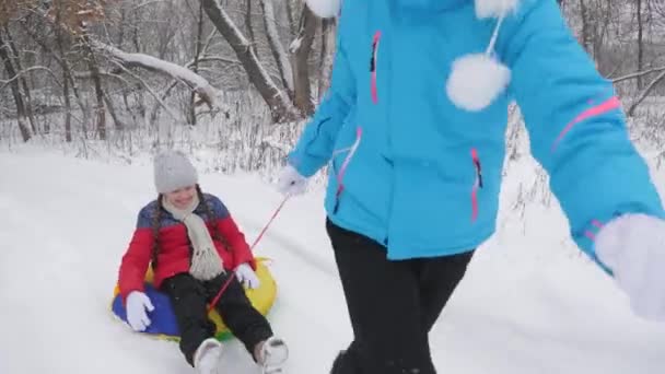 Mamá lleva a un niño feliz en un trineo en un camino nevado. Vacaciones de Navidad. Viajes y vacaciones. Entretenimiento en Tubing. Chica con un padre juega de vacaciones en el bosque — Vídeo de stock