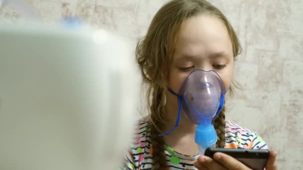 Nemocná dívka v masce vdechne lahvičku se sprejem a hraje počítačovou hru na tabletu. Dítě v modré nemocniční masce vdechuje výpary z dýchacích cest do plic. Léčba kašle. Detailní záběr — Stock video
