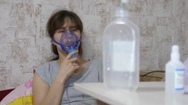 Bir hastanede yüzüne solunum maskesi takılmış bir kadın tedavi ediliyor. Hasta kız kanepede oturan bir nebulizör tarafından solunuyor. Maskeli kadın. Solunum yolu için ciğerlere buhar çek. Öksürük tedavisi