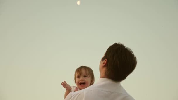 Pappa dansar på axlarna med sin dotter i solen. Far reser med baby på axlarna i solens strålar. Ett barn med föräldrarna går i solnedgången. lycklig familj vilar i parken. familjekoncept — Stockvideo