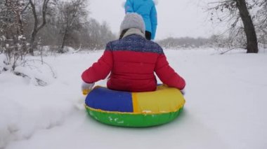 Annem mutlu bir çocuğu karlı bir yolda kızakla taşıyor. Noel tatilleri. Seyahat ve tatil. Tubing 'de eğlence. Ailesi olan bir kız ormanda tatilde oyun oynuyor.