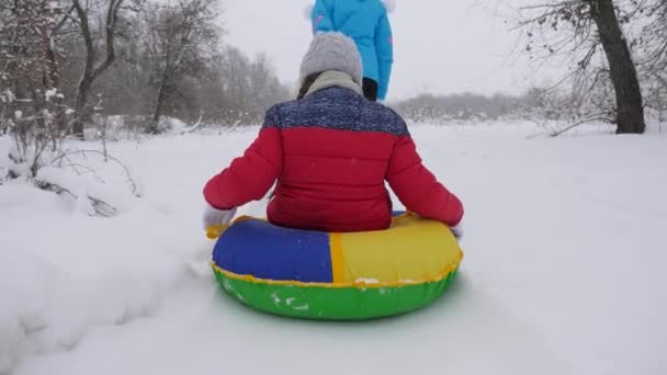 Mamma bär ett lyckligt barn på en släde på en snöig väg. Julhelger. Resor och semester. Underhållning på Tubing. Flicka med förälder leker på semester i skogen — Stockvideo