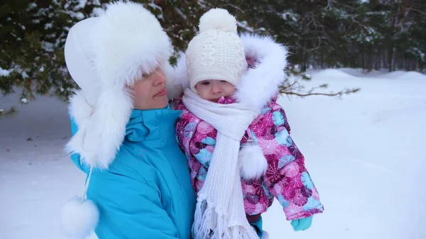 Mamma tiene la sua figlioletta e cammina lungo la strada nel parco di pini invernali innevati e ride. Weekend di Natale. Madre felice con bambino per camminare — Foto Stock