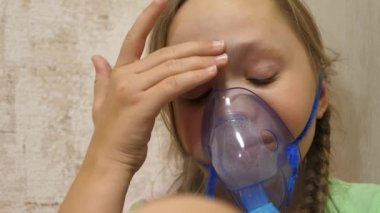 Tabletli çocuk hasta ve astım spreyinden nefes alıyor. Yakın plan. Hastanede yüzünde solunum maskesiyle tedavi edilen küçük bir kız. Yürümeye başlayan çocuk, solunum buharı soluyarak grip tedavisi görüyor..