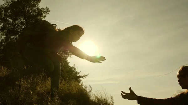 women travelers climb mountain, offer each other a helping hand, helping to climb hill. tourist teamwork. Family of tourists traveling at sunset. sisters with backpacks travel climbing mountain in sun