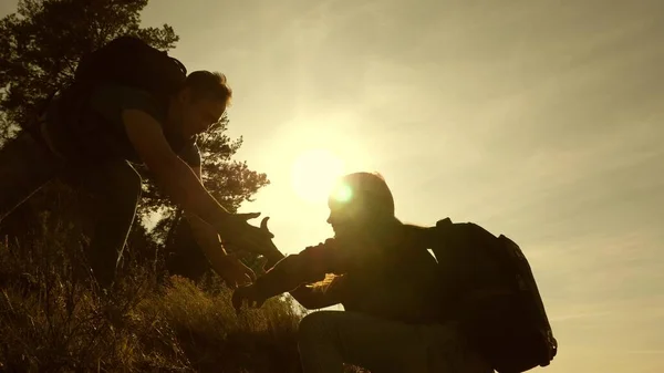 Padre tende la mano aiutando i bambini a scalare la montagna. Famiglia di turisti con bambini che viaggiano al tramonto. papà, bambini e mamma con gli zaini viaggiano scalando la montagna al sole. lavoro di squadra turistico — Foto Stock