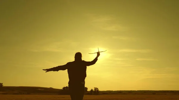 Sonho adolescente de voar e se tornar piloto. Menina feliz corre com um avião de brinquedo em um campo sob a luz do pôr do sol. As crianças brincam de avião de brinquedo. a menina quer se tornar piloto e astronauta. Movimento lento — Fotografia de Stock