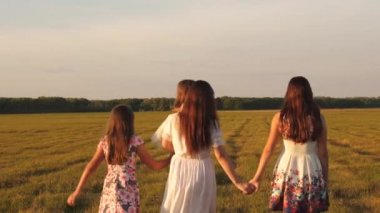 Çocuklar ve anne çayırda oynuyorlar. Mutlu aile kavramı. Parkta yürüyen kız kardeşleri olan bir anne ve küçük kız. Bir yaz tarlasında yürüyen çocuklu mutlu bir aile..