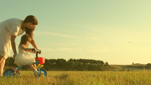 Concepto de la infancia feliz. Madre enseña a su hija a andar en bicicleta. Mamá juega con su hija pequeña. un niño pequeño aprende a andar en bicicleta . — Vídeos de Stock
