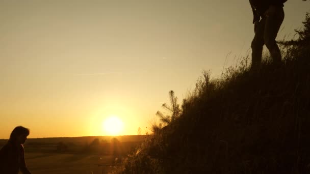 Os turistas escalam a montanha ao pôr do sol, de mãos dadas. trabalho de equipa de pessoas de negócios. O viajante estende uma mão de mulherengo a um viajante que sobe ao topo da colina. Família feliz em férias . — Vídeo de Stock