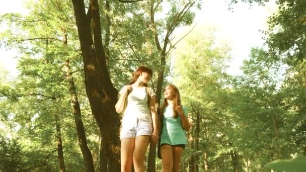 Mladé dívky s batohy v lese procházejí houštinami. Hiker, chodí do lesa. šťastná dívka v letním parku. puberťankou dobrodružství na dovolené. — Stock video