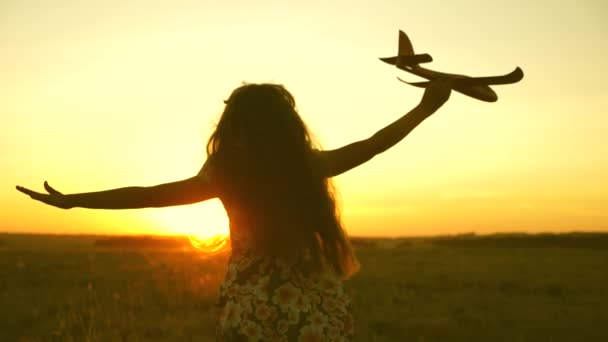 Chica feliz corre con un avión de juguete en un campo en la luz del atardecer. niños juegan juguete avión. adolescente sueña con volar y convertirse en piloto. la chica quiere convertirse en piloto y astronauta. Movimiento lento — Vídeos de Stock