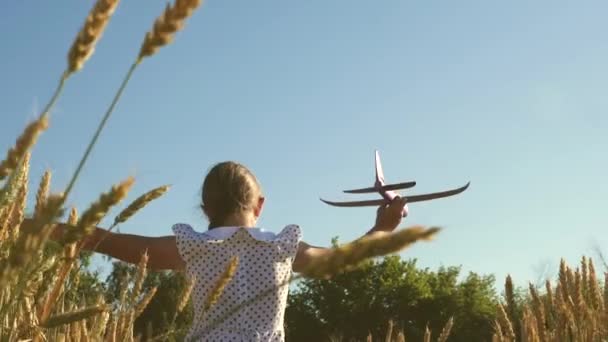 Lycklig flicka springer med ett leksaksplan på ett fält i solnedgångens sken. Barn leker leksaksflygplan. Tonåringen drömmer om att flyga och bli pilot. Flickan vill bli pilot och astronaut. Långsamma rörelser — Stockvideo