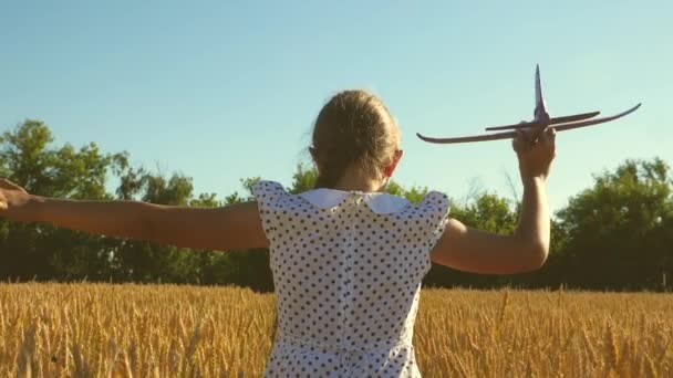 Ragazza felice corre con un aeroplano giocattolo su un campo alla luce del tramonto. i bambini giocano aereo giocattolo. adolescente sogna di volare e diventare pilota. la ragazza vuole diventare pilota e astronauta. Rallentatore — Video Stock