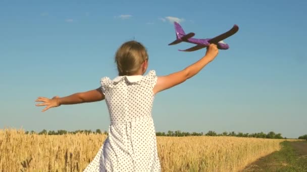 Chica feliz corre con un avión de juguete en un campo en la luz del atardecer. niños juegan juguete avión. adolescente sueña con volar y convertirse en piloto. la chica quiere convertirse en piloto y astronauta. Movimiento lento — Vídeo de stock