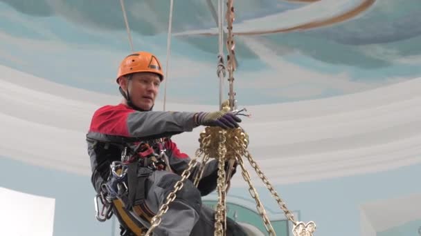 Een industriële klimmer op een ladder bereidt een touw voor op het hijsmateriaal. een werknemer met een beschermhelm breit een knoop aan een touw. — Stockvideo