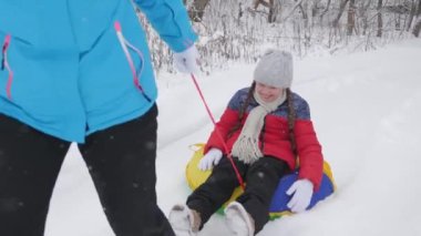 Mutlu anne, beyaz karlı bir yolda kızakla bir çocuğa biniyor. Noel tatilleri. Yetişkinler ve çocuklar için eğlenceli bir oyun. Mutlu aile kavramı. Bir genç Tubing 'e biniyor.