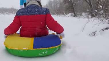 Annem mutlu bir kızı beyaz ve karlı bir yolda kızakla taşıyor. Çocuk bir boruya biniyor ve kahkahalarla dolu. Noel tatilleri. Aileyle hafta sonu. Mutlu aile kavramı.